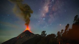 A photo of a volcano erupting at night with the Milky Way visible in the sky