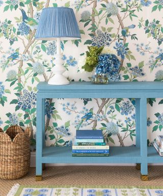 Corner of living room, floral wallpaper, blue side table, blue table lamp, books and ornaments