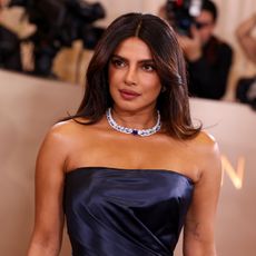 a woman with brown hair wears a strapless blue gown and poses at a red carpet event