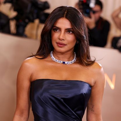 a woman with brown hair wears a strapless blue gown and poses at a red carpet event