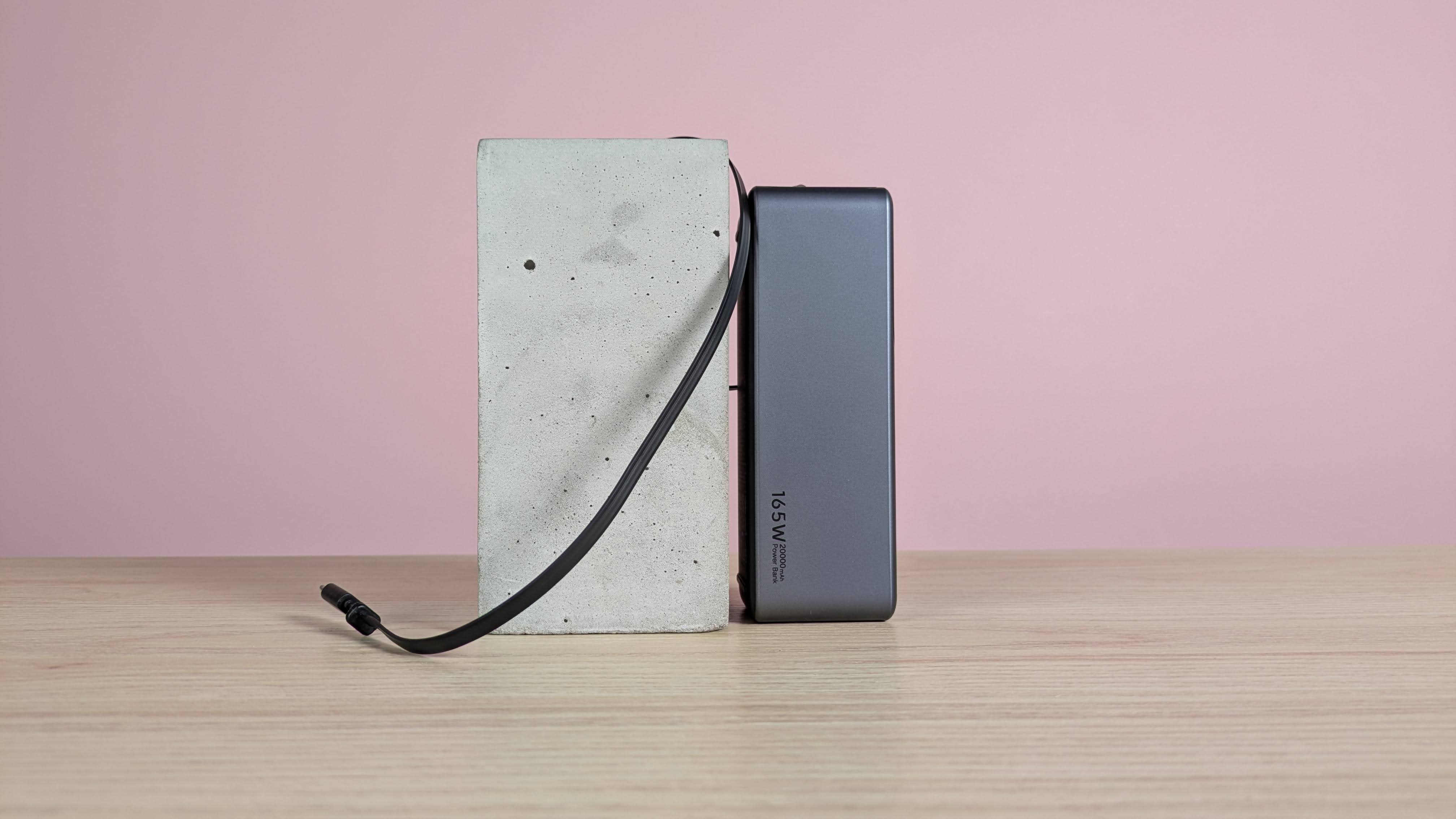 Ugreen Nexode Power Bank 20000mAh 165W leaning on plinth with in-built USB-C cable pulled out, on desk with pink background
