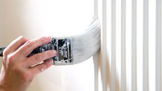 Hand holding paintbrush painting radiator
