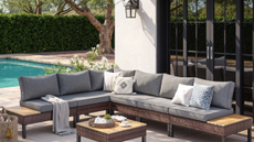 a backyard with a large sectional couch with gray cushions, a small coffee table, and a pool in the background