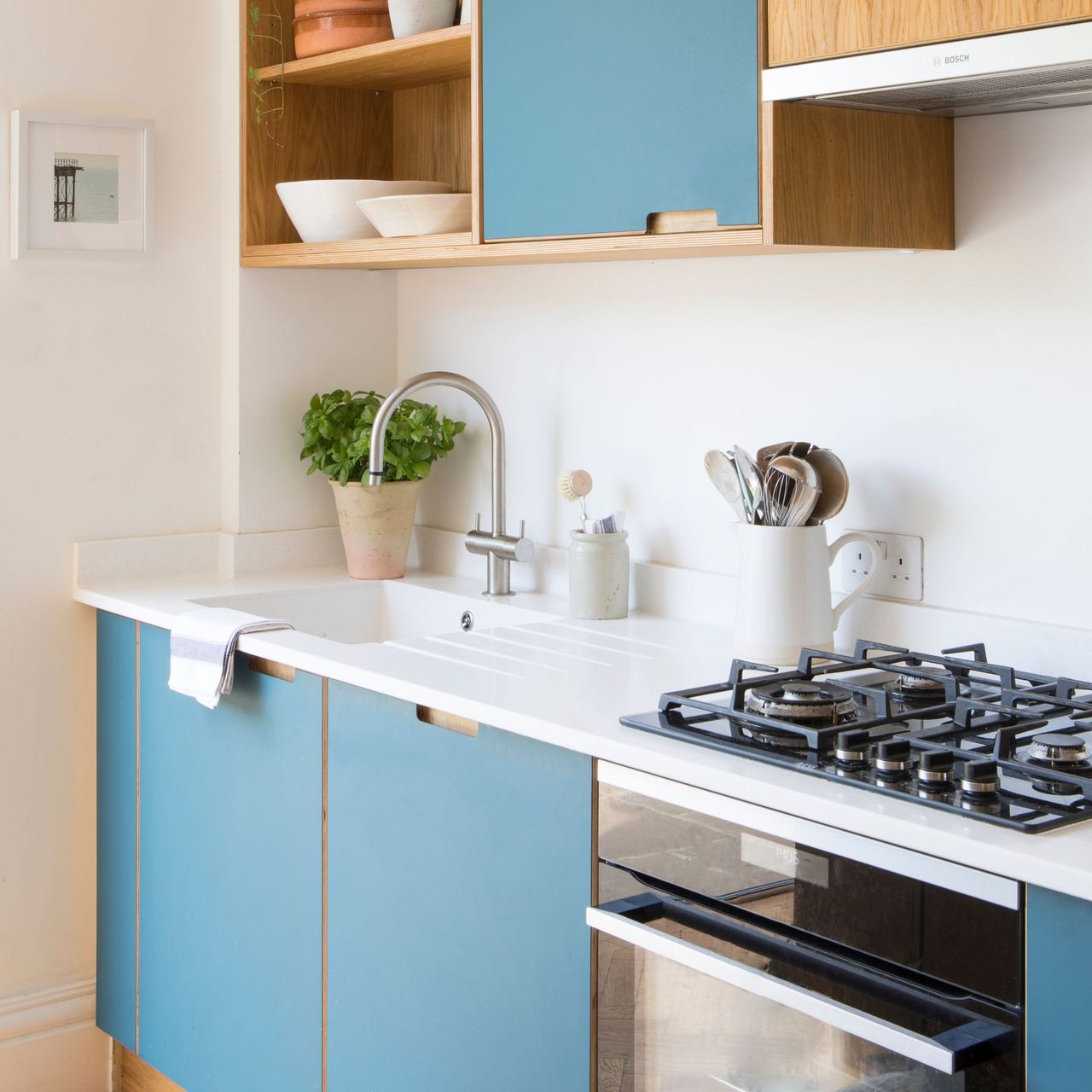 Kitchen with blue cabinets and white worktops, and a oven with a gas hob on top 
