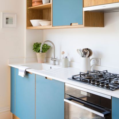 Kitchen with blue cabinets and white worktops, and a oven with a gas hob on top