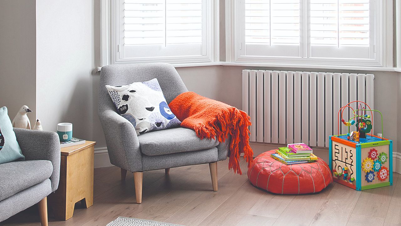 A grey living room with a red pouffe and an activity toy box next to it