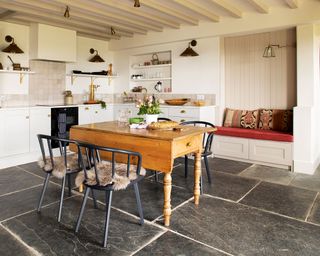 white kitchen with pine table and flagstones and painted beams and built-in bench seat