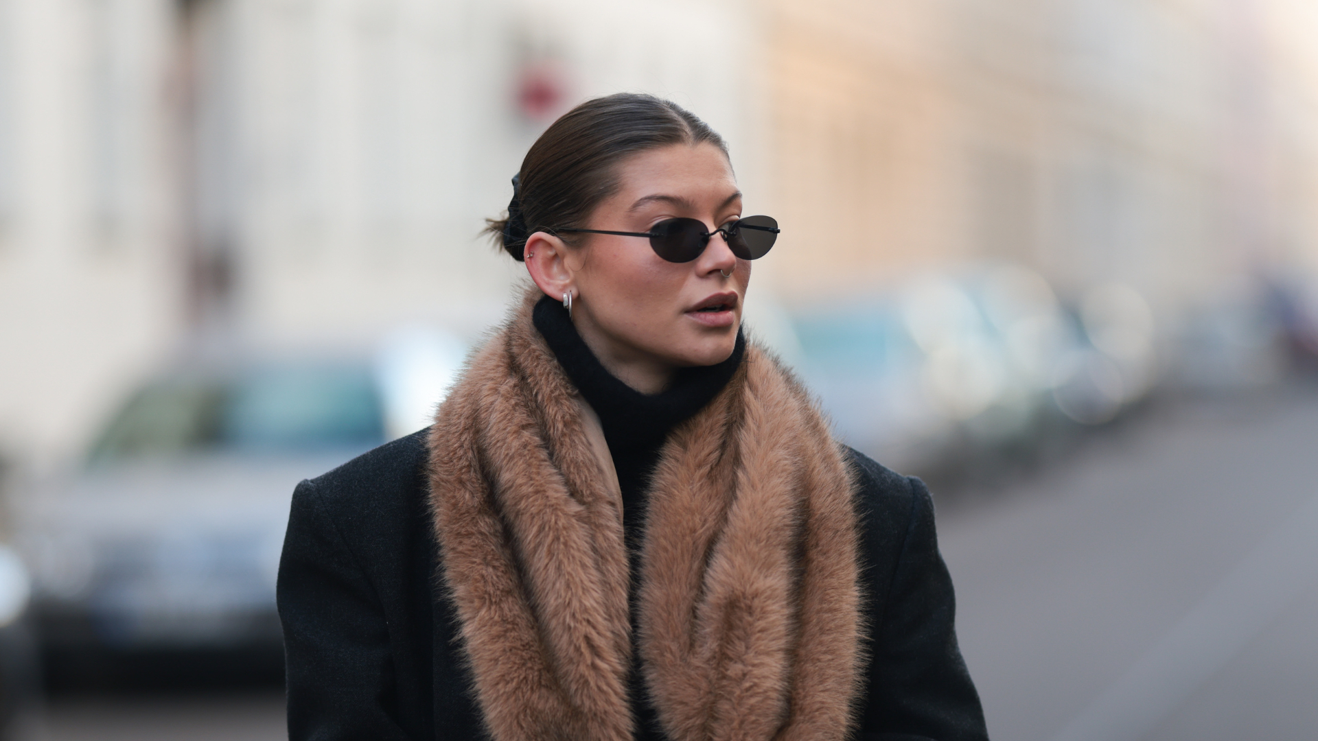 Sophia Geiss seen wearing dark wide-leg Closed jeans paired with chunky black Prada boots. The outfit features a fitted black top from &amp; Other Stories layered under a long, structured black Herskind coat. A soft, voluminous faux-fur Mango scarf in warm brown tones adds texture and contrast. Accessories include a black YSL handbag with gold hardware and sleek oval sunglasses from Vehla Eyewear. The look combines modern minimalism with luxurious vintage-inspired elements on November 22, 2025 in Berlin, Germany