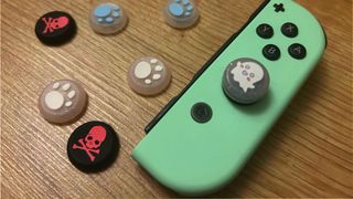 A pastel green JoyCon with a glittery ghost thumb grip, surrounded by other colorful grips depicting punk skulls and paw prints