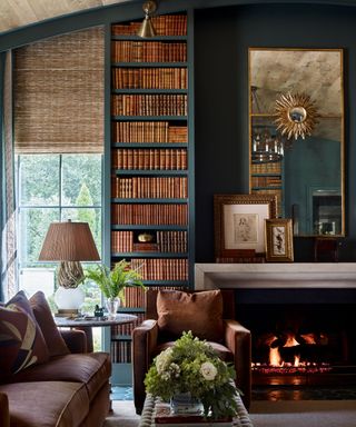 living room with a teal wall, large built-in bookshelves, fireplace, large brass mirror above, and traditional decor