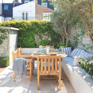 Patio with wooden dining set and concrete bench surrounded by plants and a shed