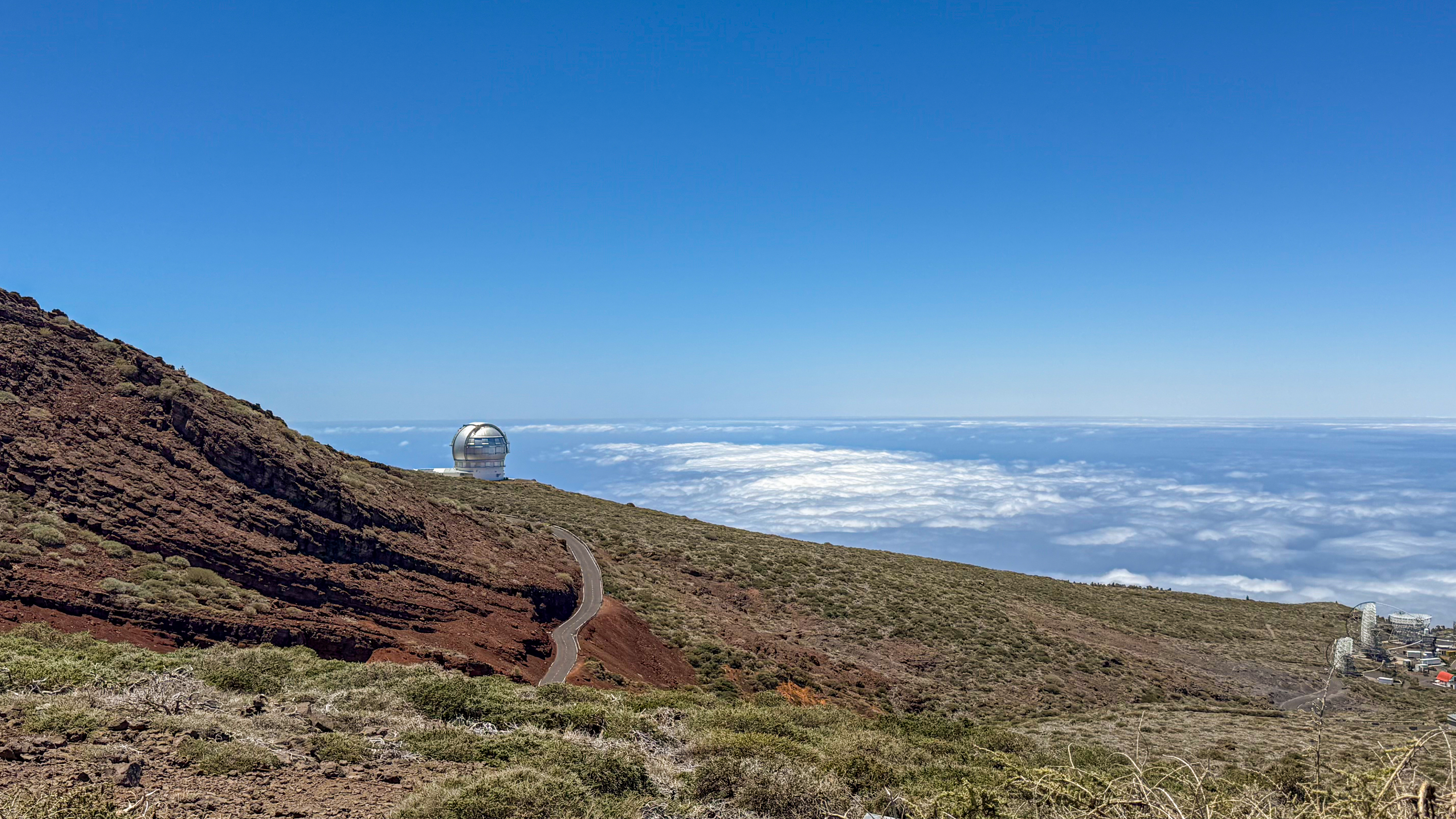 starmus la palma 2025 trip to Roque de los Muchachos, shows a winding road and an observatory with a dome against a blue sky and clouds below.