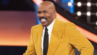 Steve Harvey smiles while wearing a yellow suit jacket on Celebrity Family Feud in 2024.