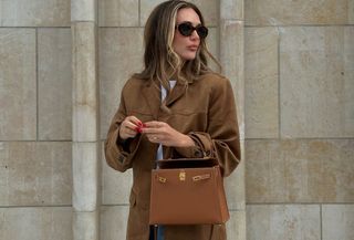 Woman wearing a tan suede coat and oval sunglasses.