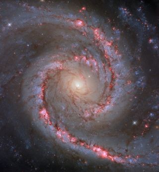 A view of a spiral structure that has red specks, blue specks and a glowing yellowish core.