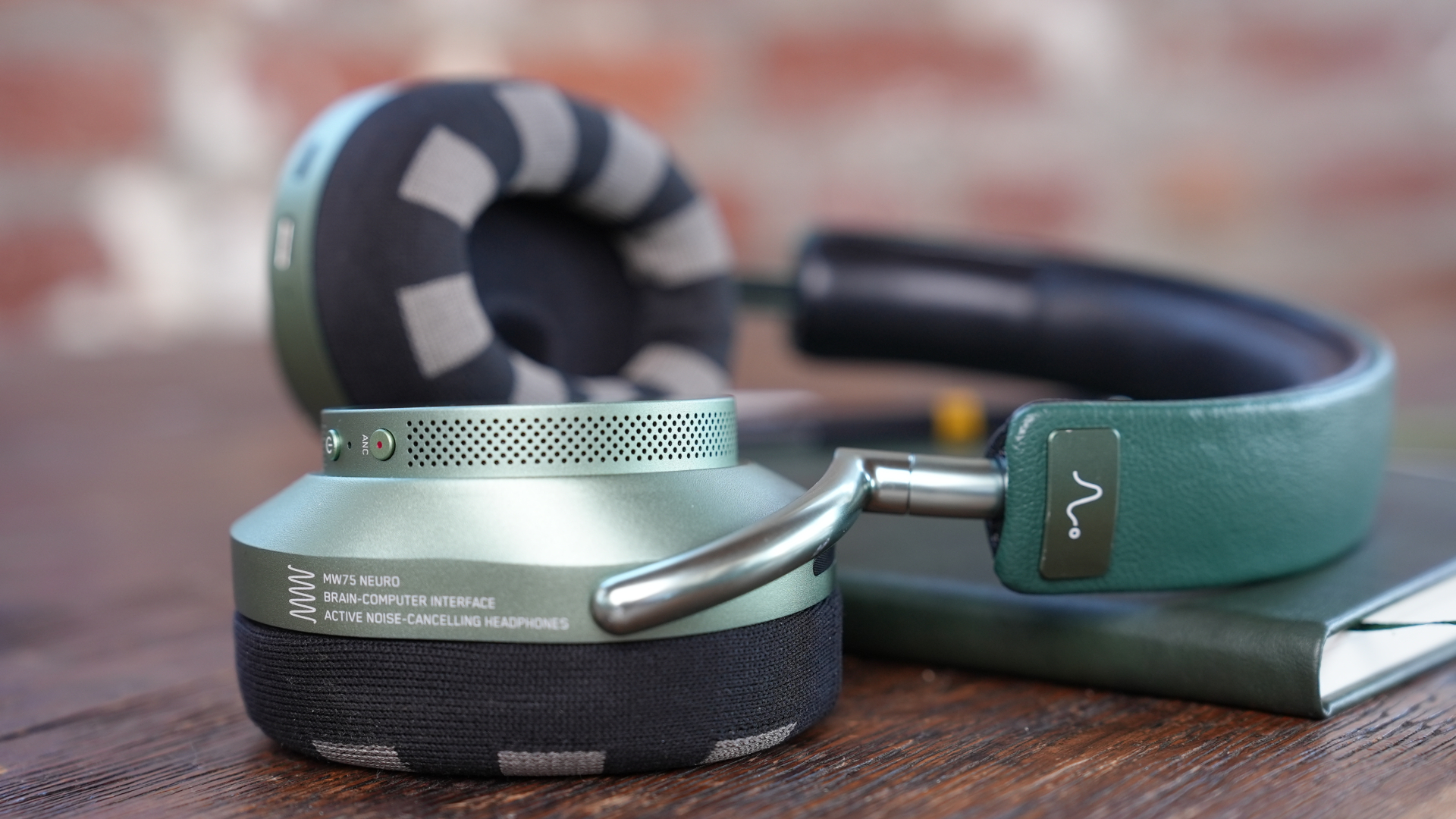 Neurable MW75 LT in green on a wooden table, with an exercise book