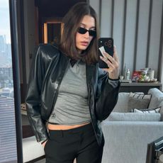 Hailey bieber wears a black leather jacket with a gray top and black pants.