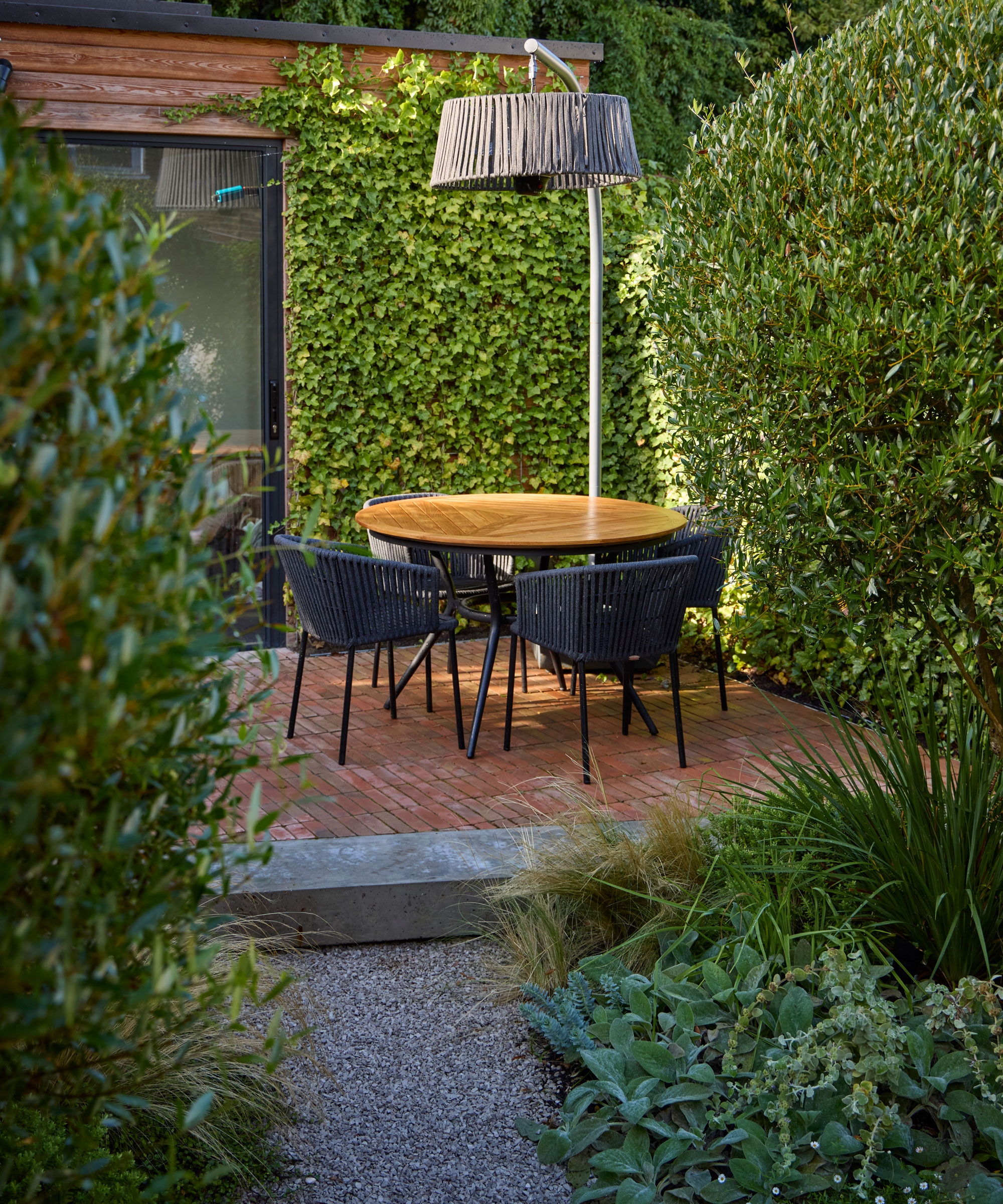 small patio garden with gravel path and silver foliage plants, with garden furniture and hedge