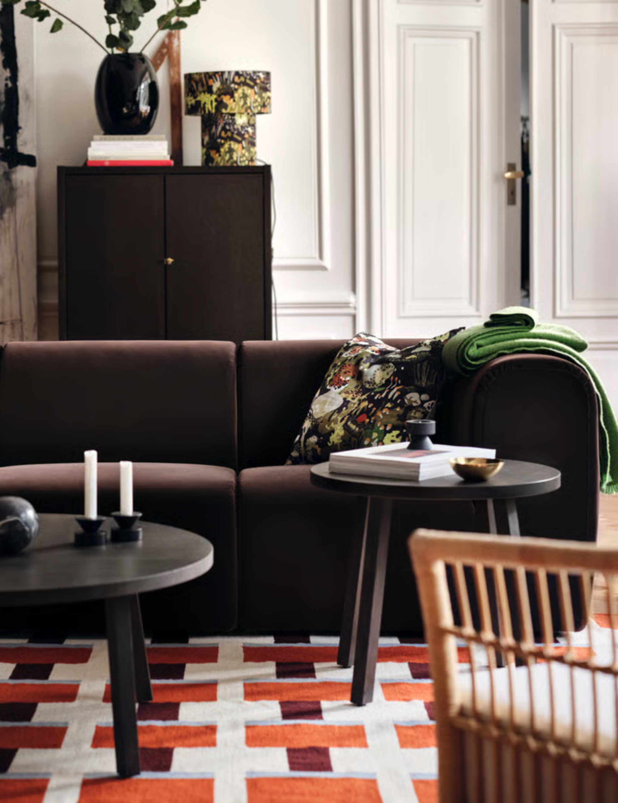 Eclectic living room featuring a terracotta, oxblood, and blue geometric rug, playful decor, and a chocolate brown Stockholm Sofa by IKEA.