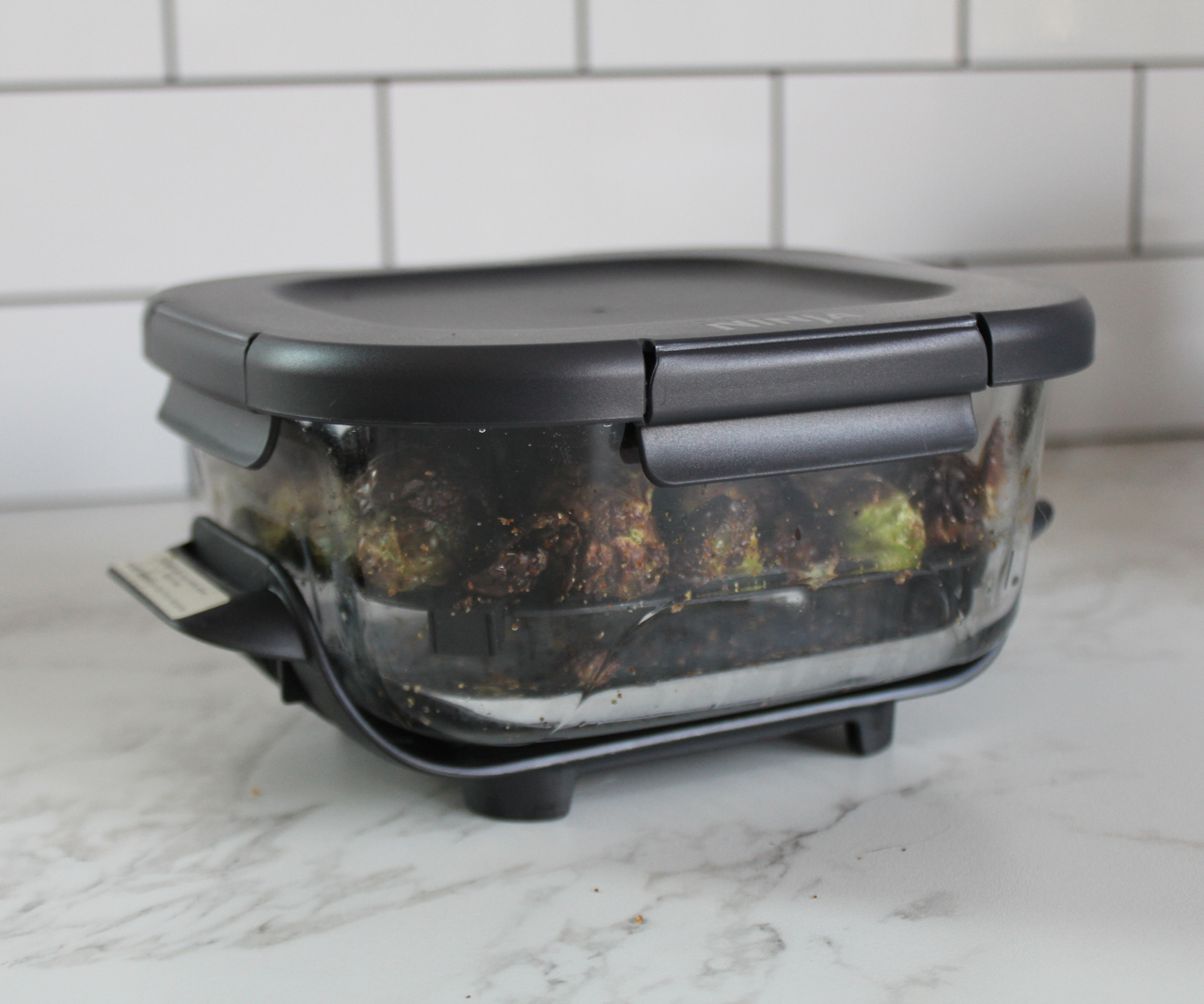 A glass baking dish with a black plastic lid on a marble kitchen counter.