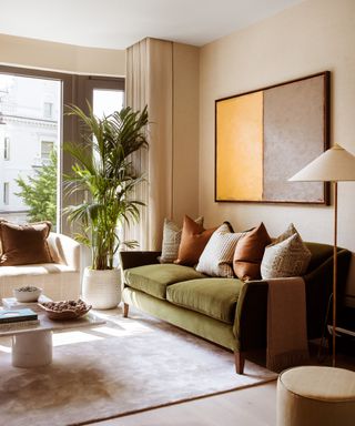 A neutral living room with large windows and a green velvet sofa
