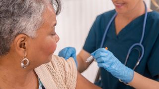 nurse prepares to give older female patient a shot in her upper arm