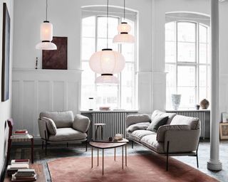 A contemporary couch and matching armchair with minimal black metal frame and gray upholstery, three lantern pendants, red rug