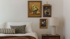 Close-up image of a bed with no bedframe in a white bedroom. There are two throw pillows and a throw blanket on the bed, and three paintings near the bedside table.