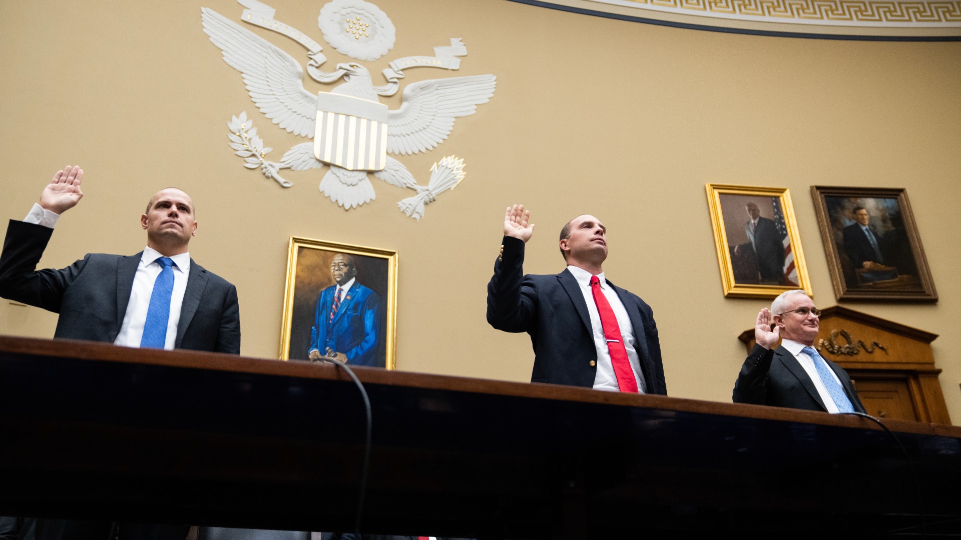 three men in suits raise their right hands under a seal of the us government