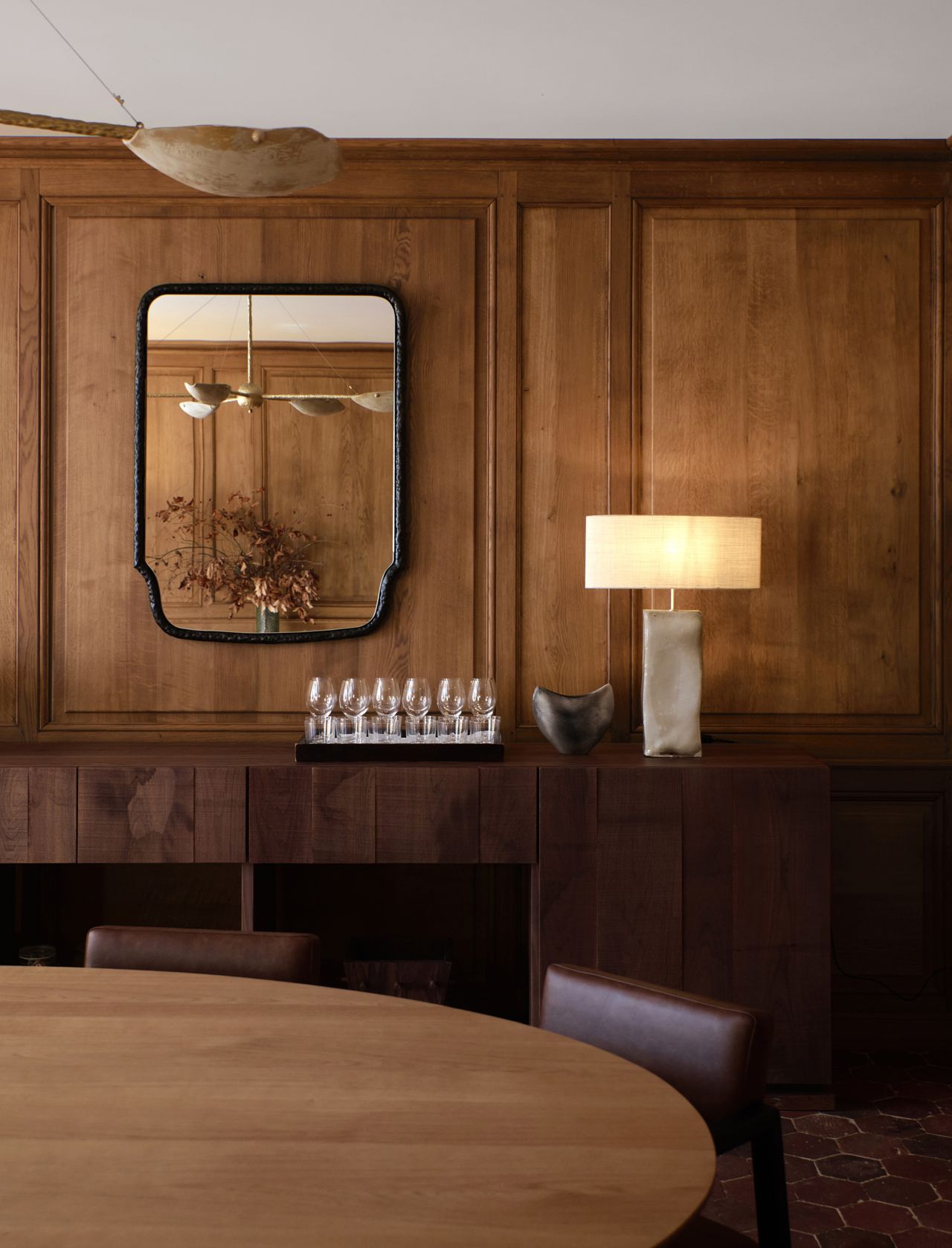 A clad-in-wood restaurant dining room blends nostalgic decor, like wood-paneled walls, with modern touches, from shapely mirrors to a softly glowing table lamp.