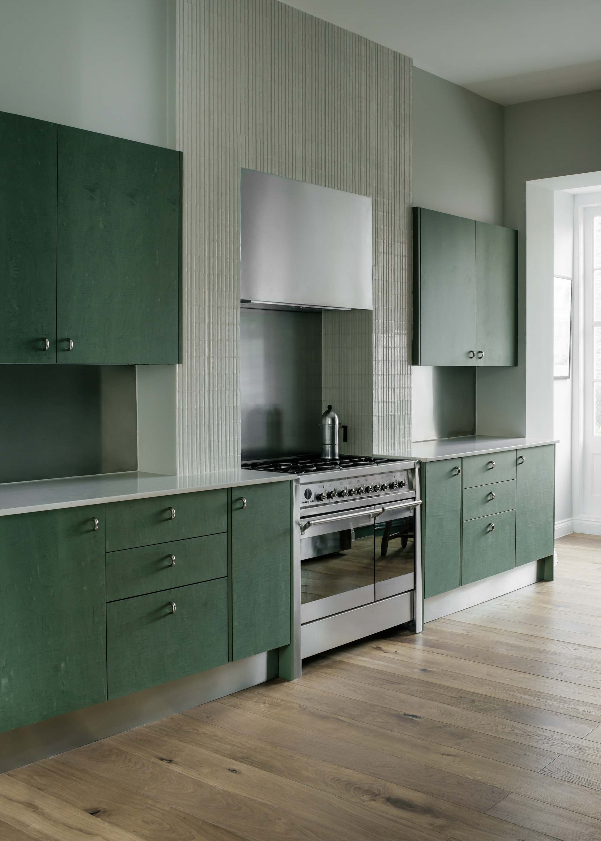 Image of a green kitchen with dark, teal-tinted green cabinets with powder green-blue walls and wooden floors.
