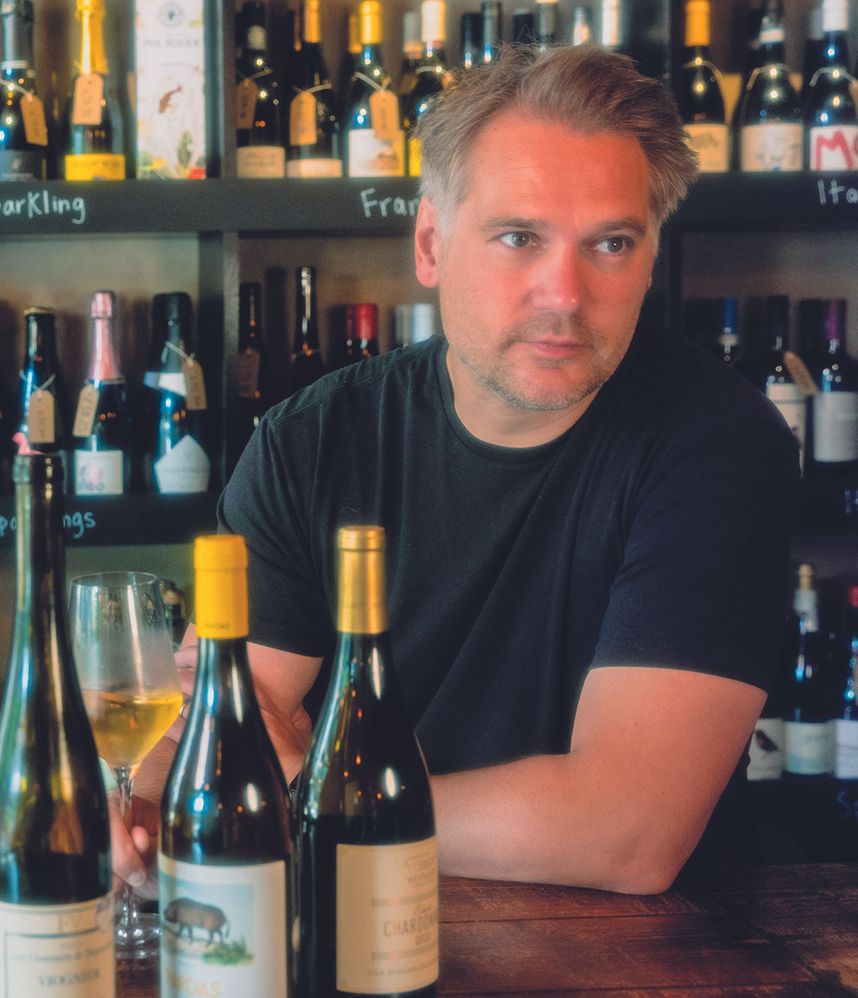 Man sat a table with a glass of wine and three wine bottles
