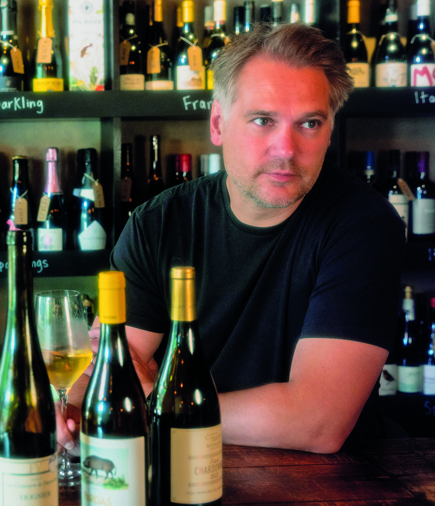 Man sat a table with a glass of wine and three wine bottles