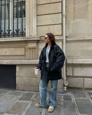 @deborabrosa wears blue jeans, a waxed jacket, a grey jumper and light brown suede trainers