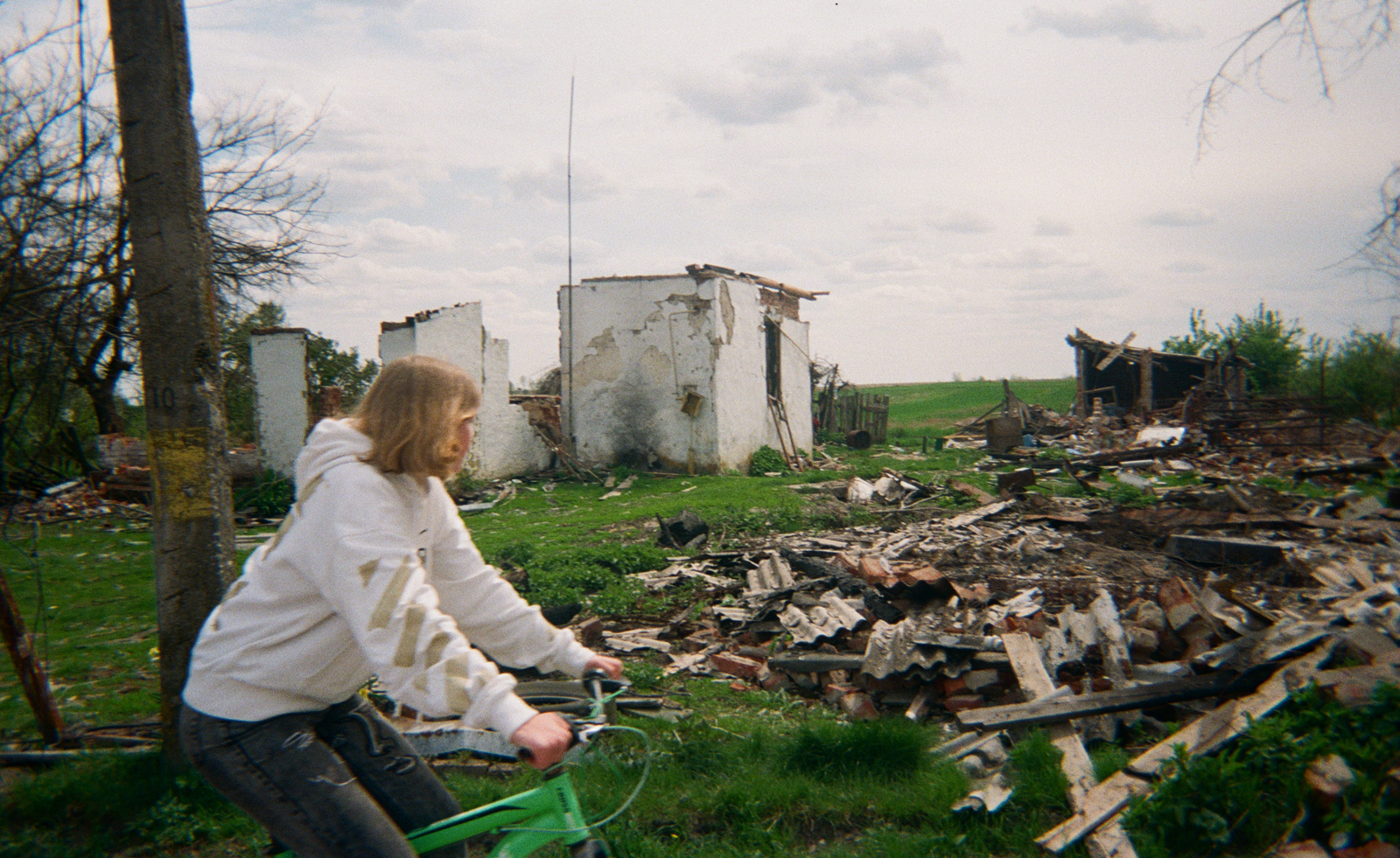 Ukrainian child riding bike past ruins