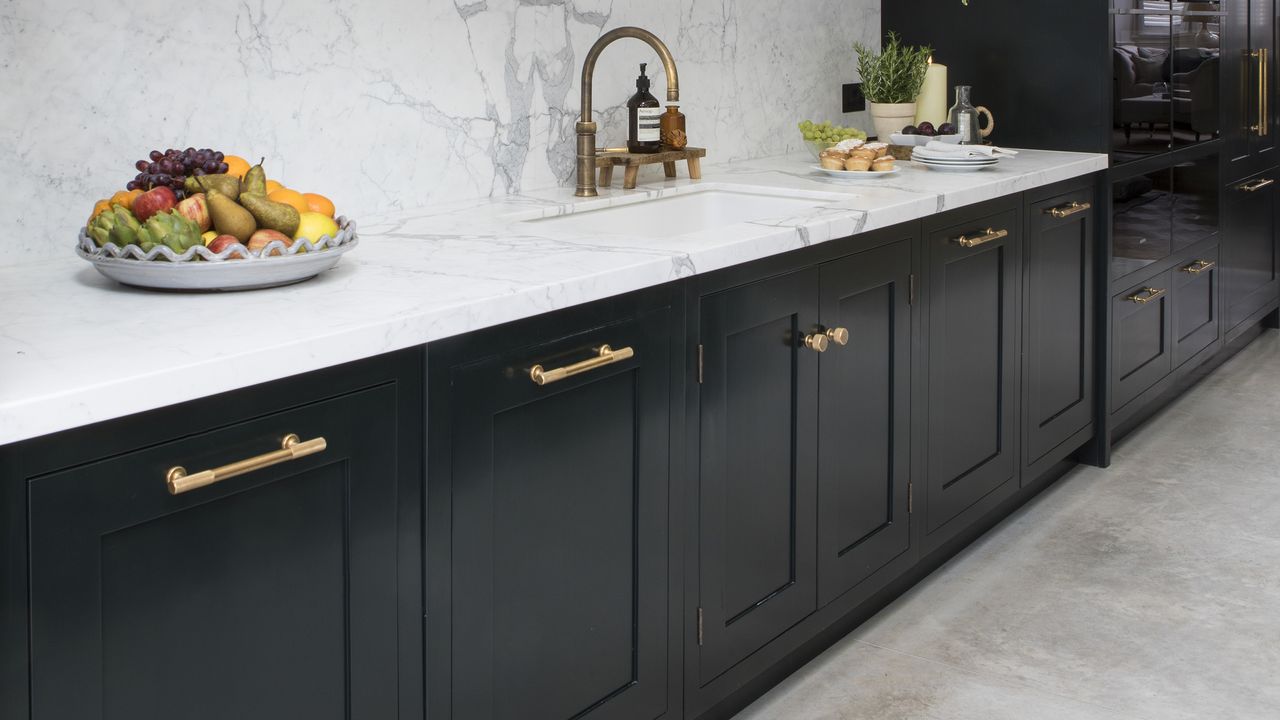 Black kitchen with cupboards, white worktops and brass handles.