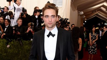 Robert Pattinson stands with hands in pockets on the red carpet.