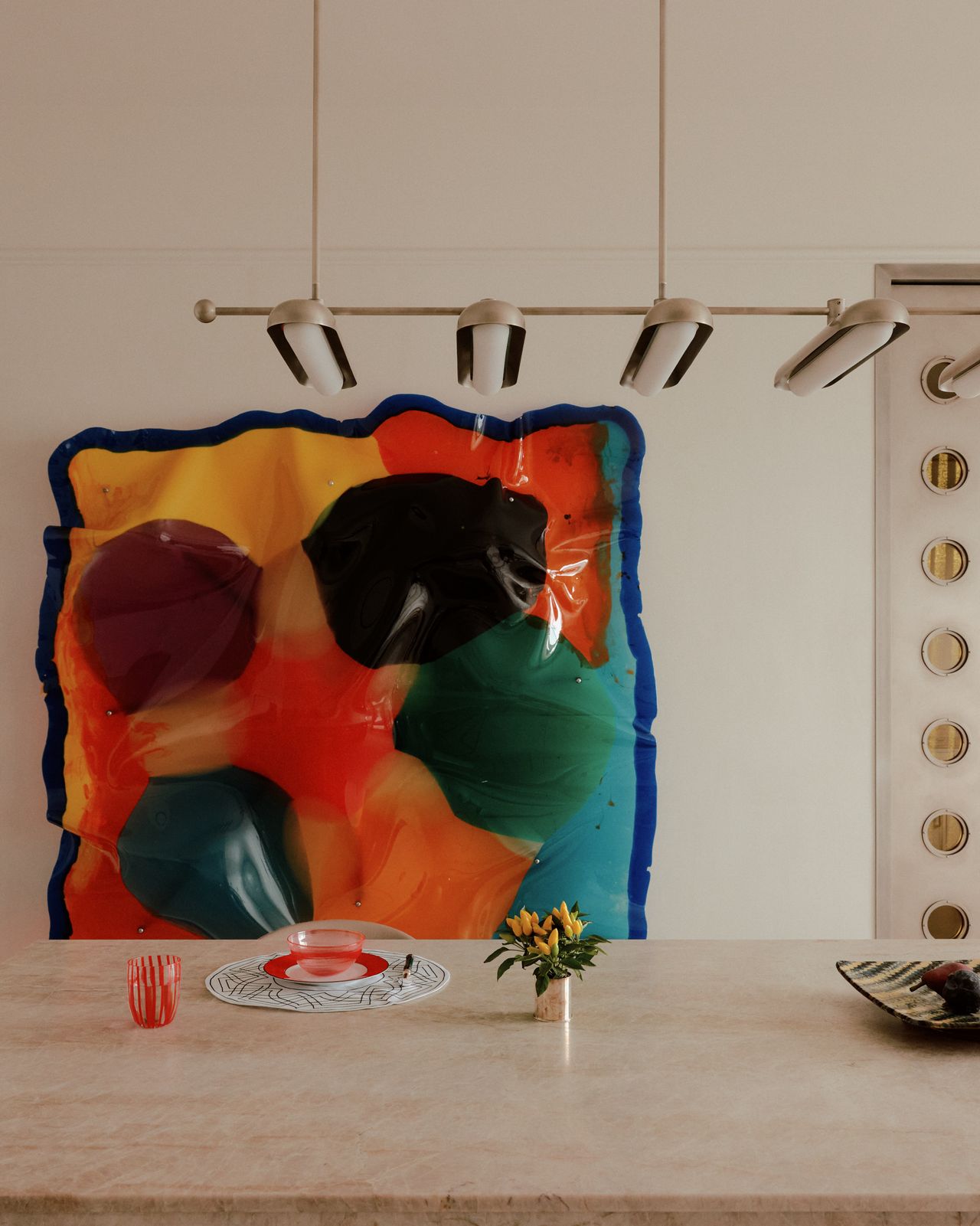 bold artwork on the wall in neutral kitchen with pendant light over the island bench and plates and cup styled on the counter