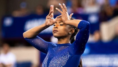 Gymnast Nia Dennis raises her hands to her head in a flourish during a performance.