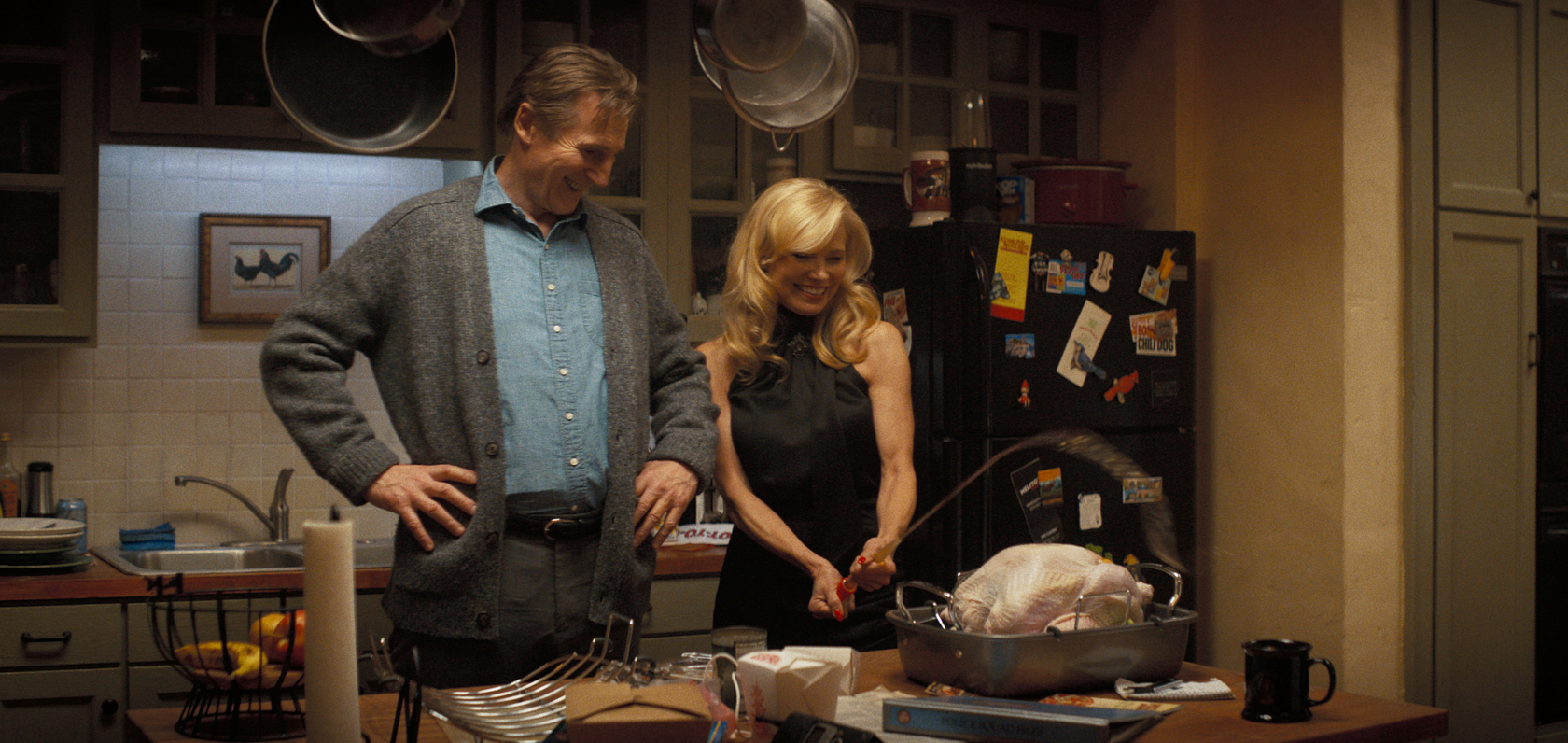 Liam Neeson smiles as Pamela Anderson shoots a turkey baster over an uncooked bird in The Naked Gun (2025). 