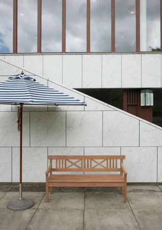 A white and blue striped parasol with a wooden bench under it in front of a staircase.