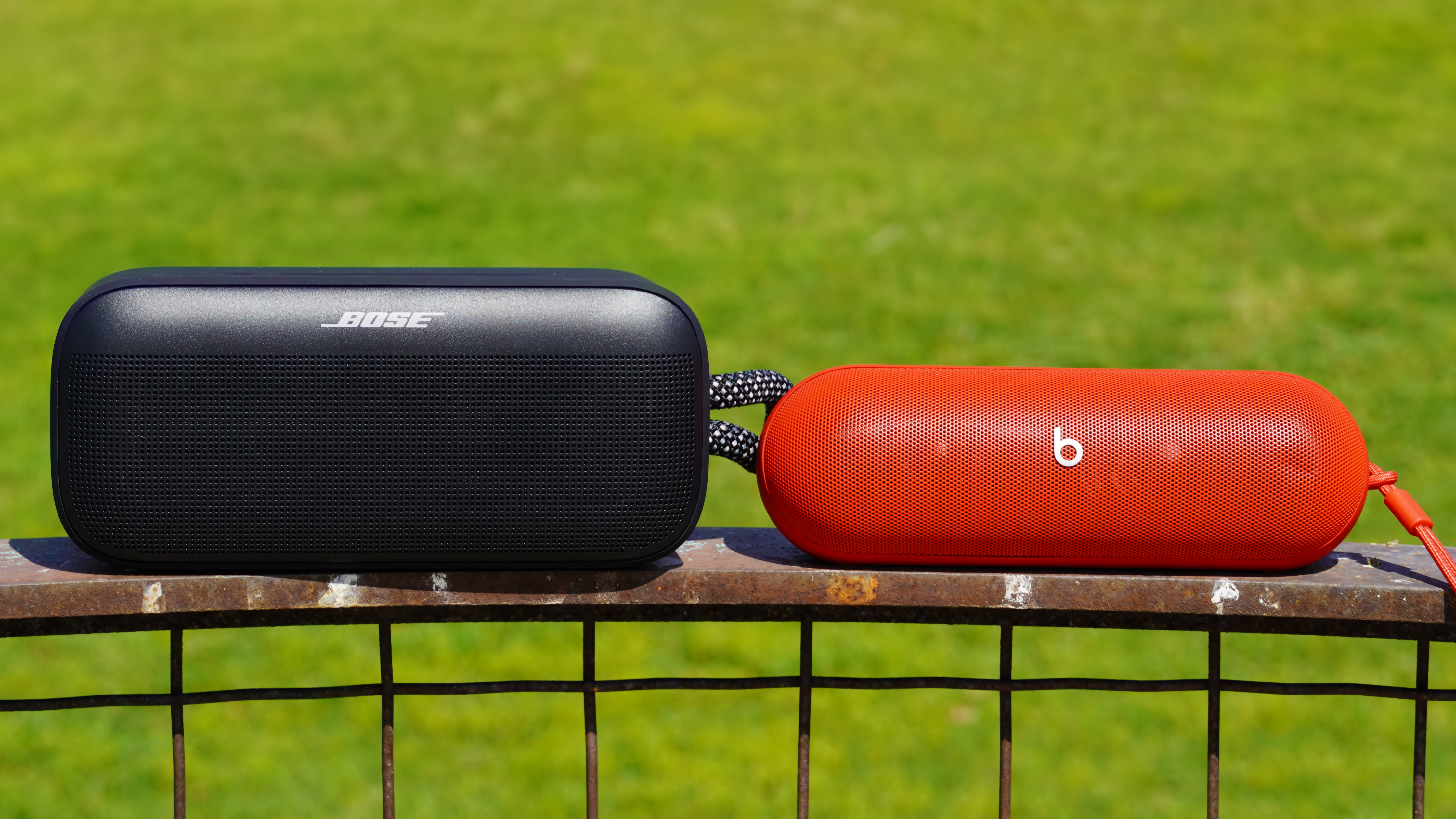 The Bose SoundLink Plus (black) beside the Beats Pill (red) on a railing.