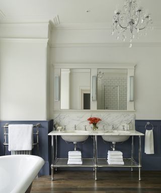 A bathroom with a chandelier, blue paneling and double vanity