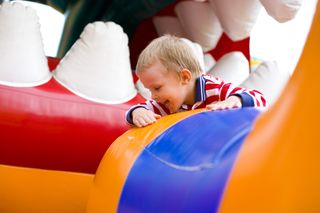 A close-up of a young blonde boy smiling whilst on a bouncy castle.