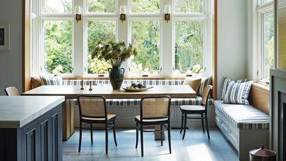 a light and bright kitchen dining area with a striped large banquette, ceiling beams and blue tiled floor