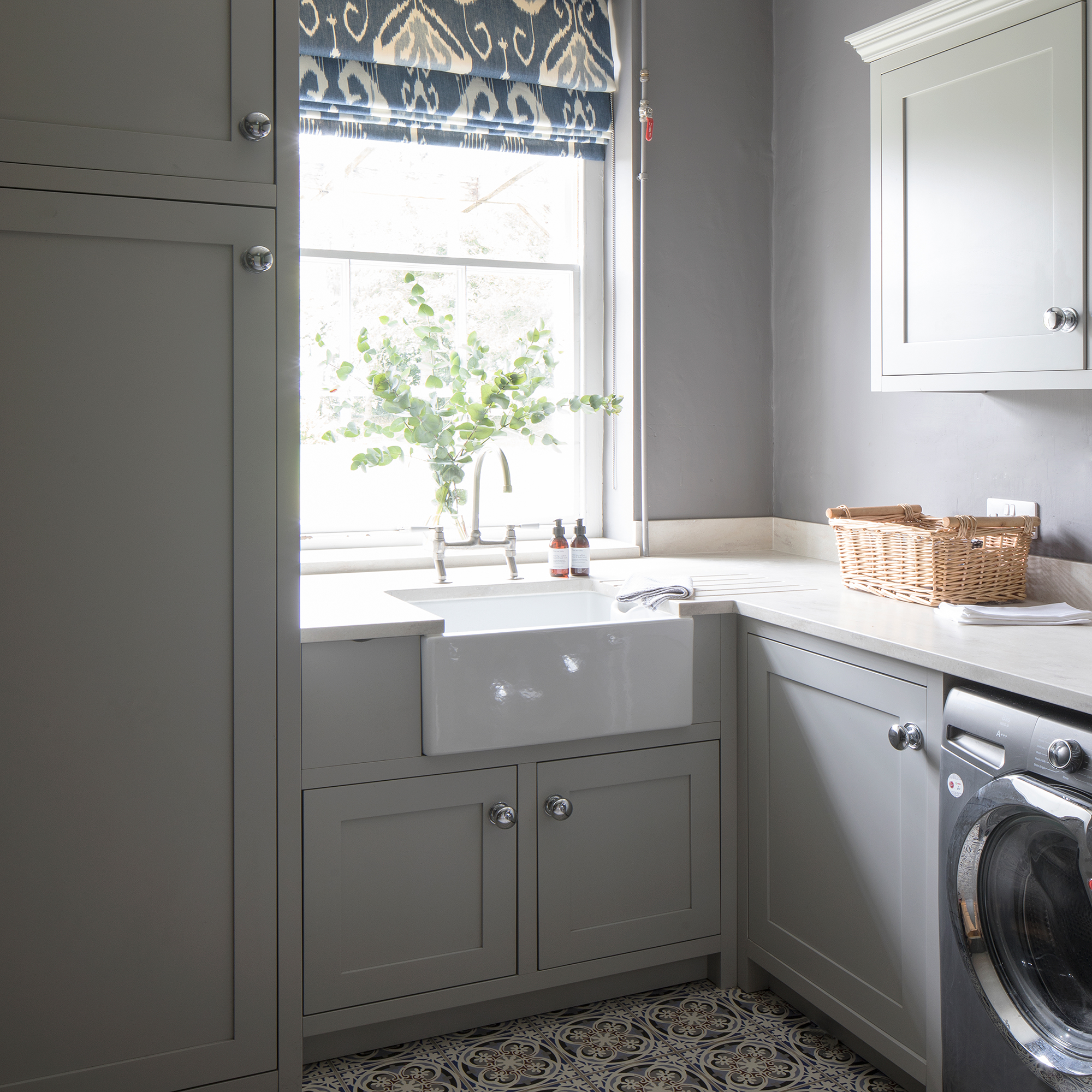 Grey utility room with Belfast sink, patterned tiled floor and patterned window blind
