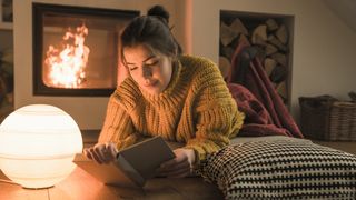Best light therapy lamps: A woman in a mustard color knitted jumper reads a book next to a sun lamp