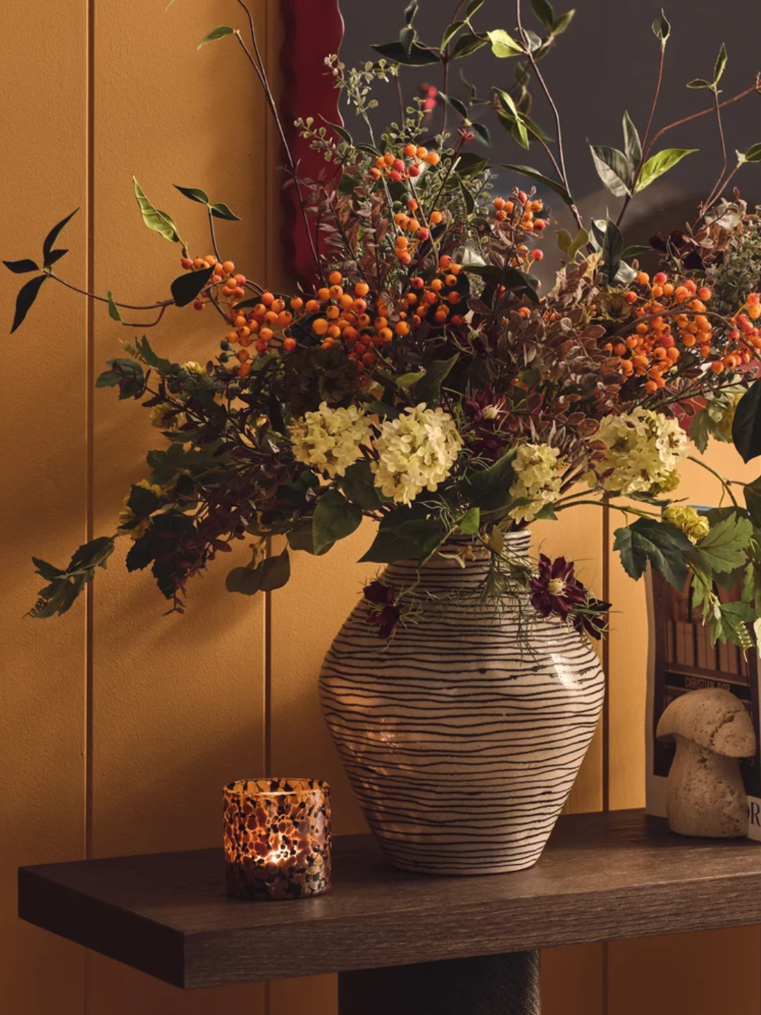 A black and white striped vase from OKA styled with flowers and a scented candle