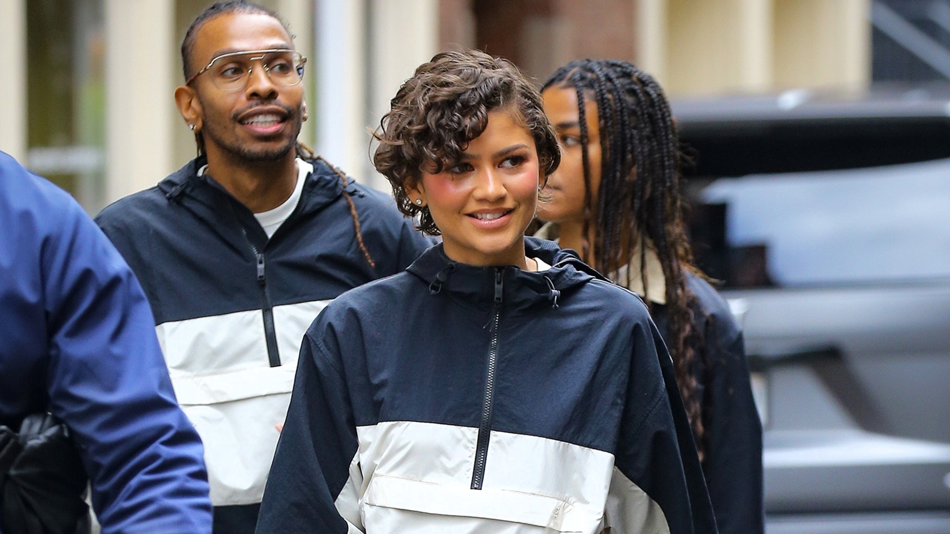 Zendaya wearing a navy and white windbreaker jacket, navy pants, and burgundy sneakers.