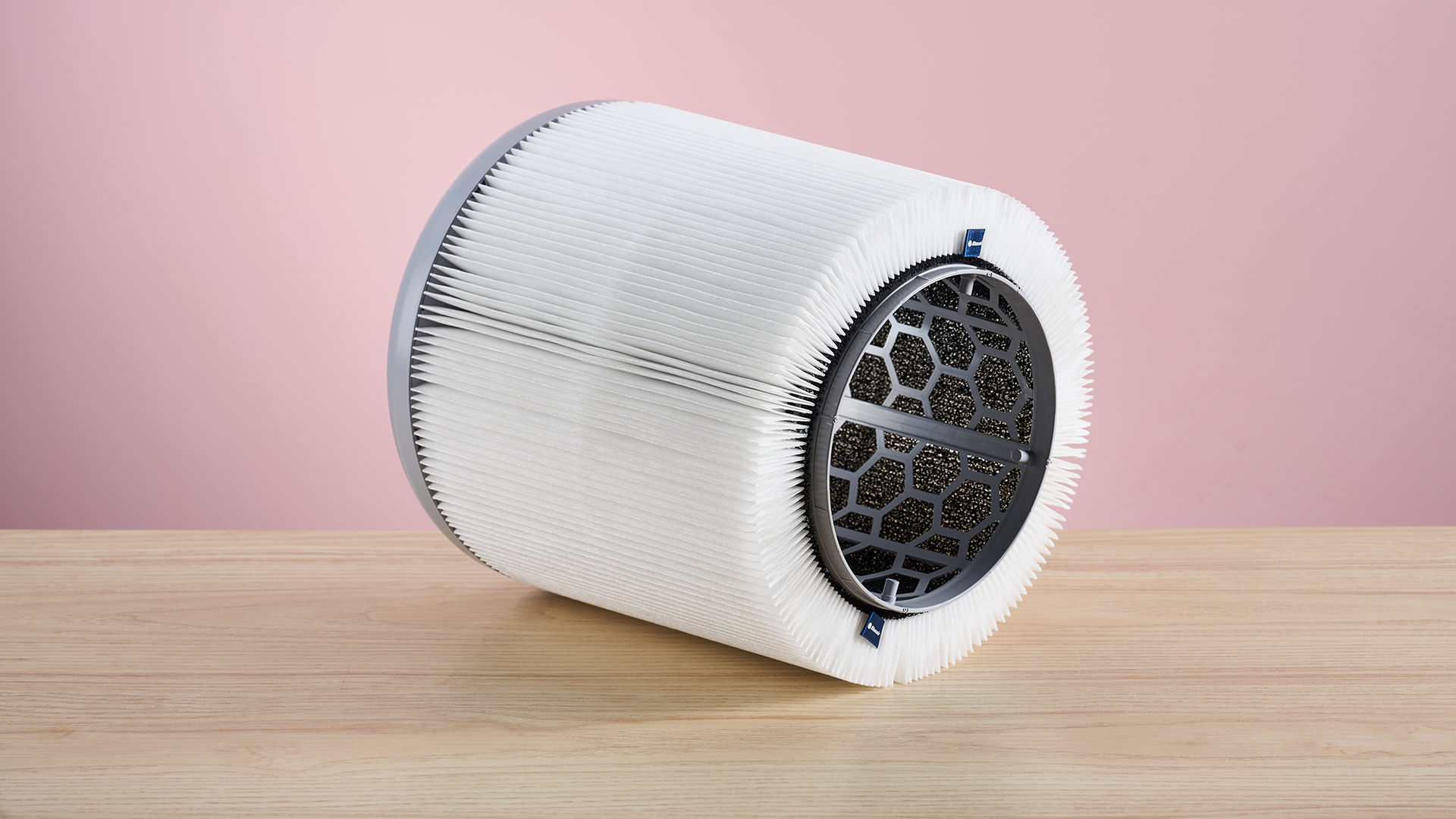 The HEPA filter from inside the Blueair air purifier sits facing forward on a wood surface against a pink background.